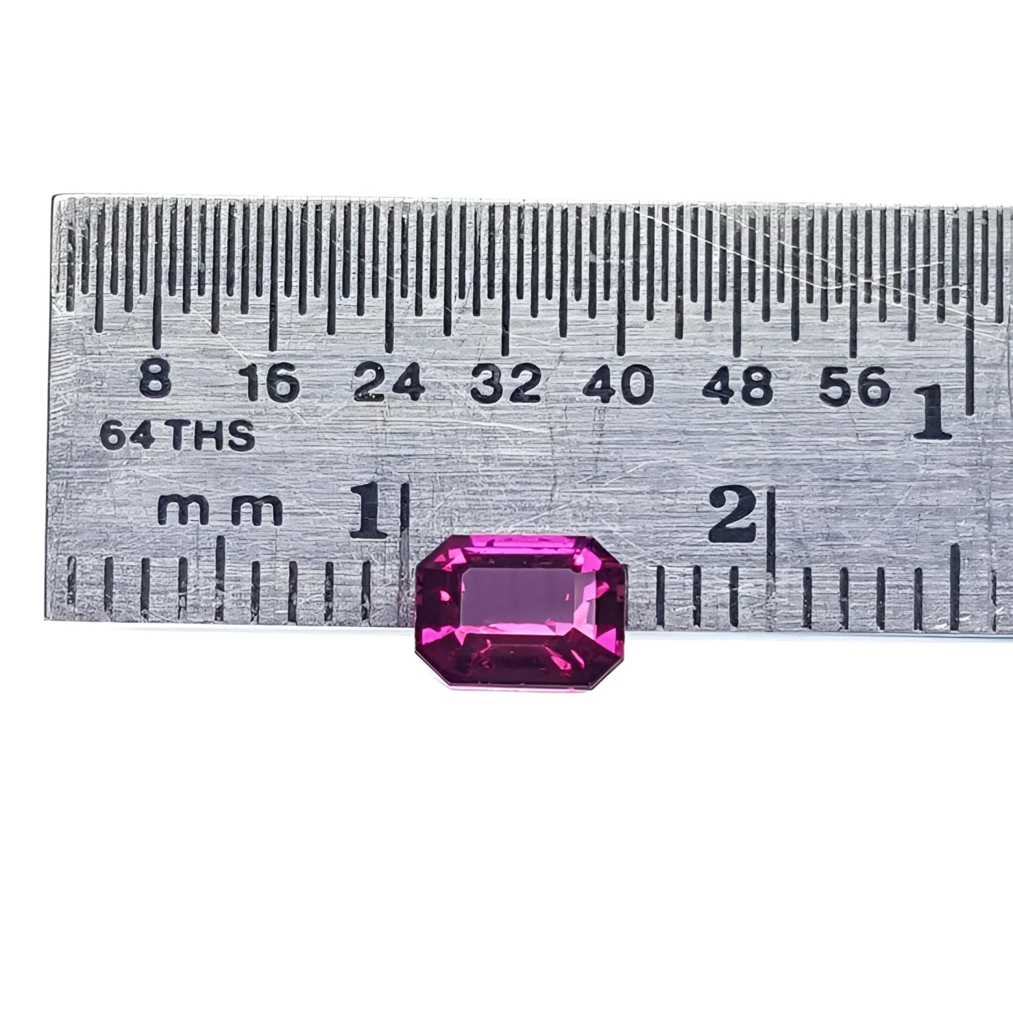 Vibrant, deep reddish-pink, emerald-cut natural ruby next to a ruler for size reference.