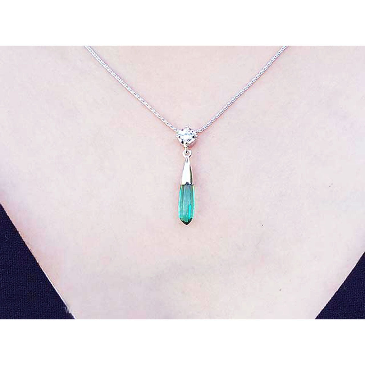 A woman wearing an emerald and diamond briolette necklace in 14k white gold with a natural diamond