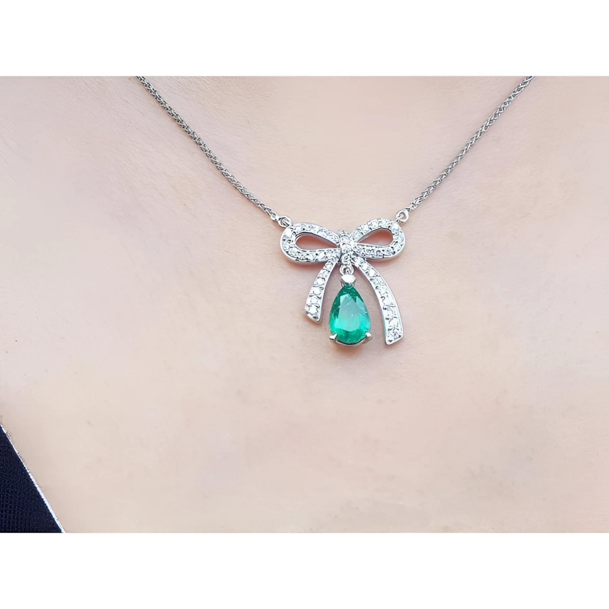 18K white gold bow-tie necklace with pear-shaped emerald and diamonds on a chain.