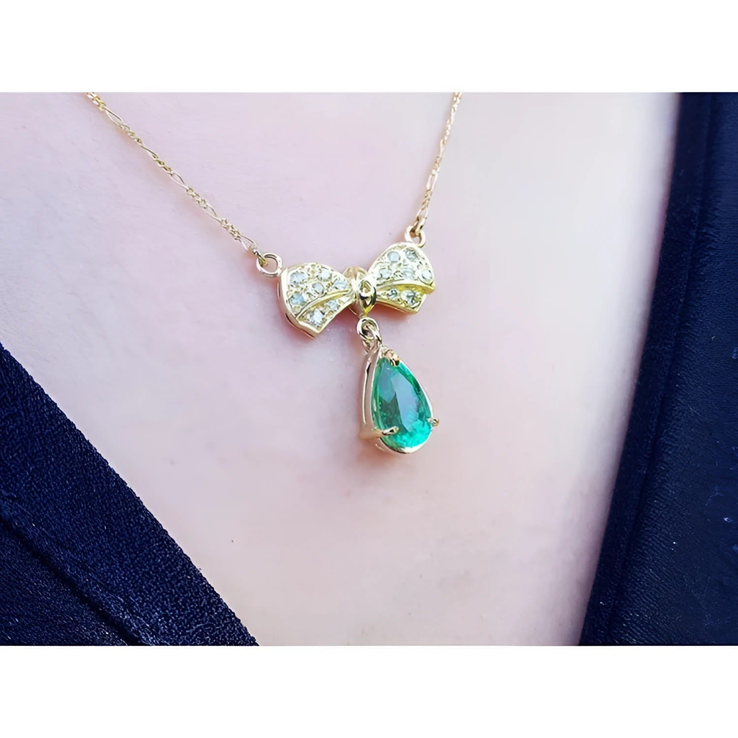 18K yellow gold bow-tie necklace with pave diamonds and a dangling pear-shaped emerald.