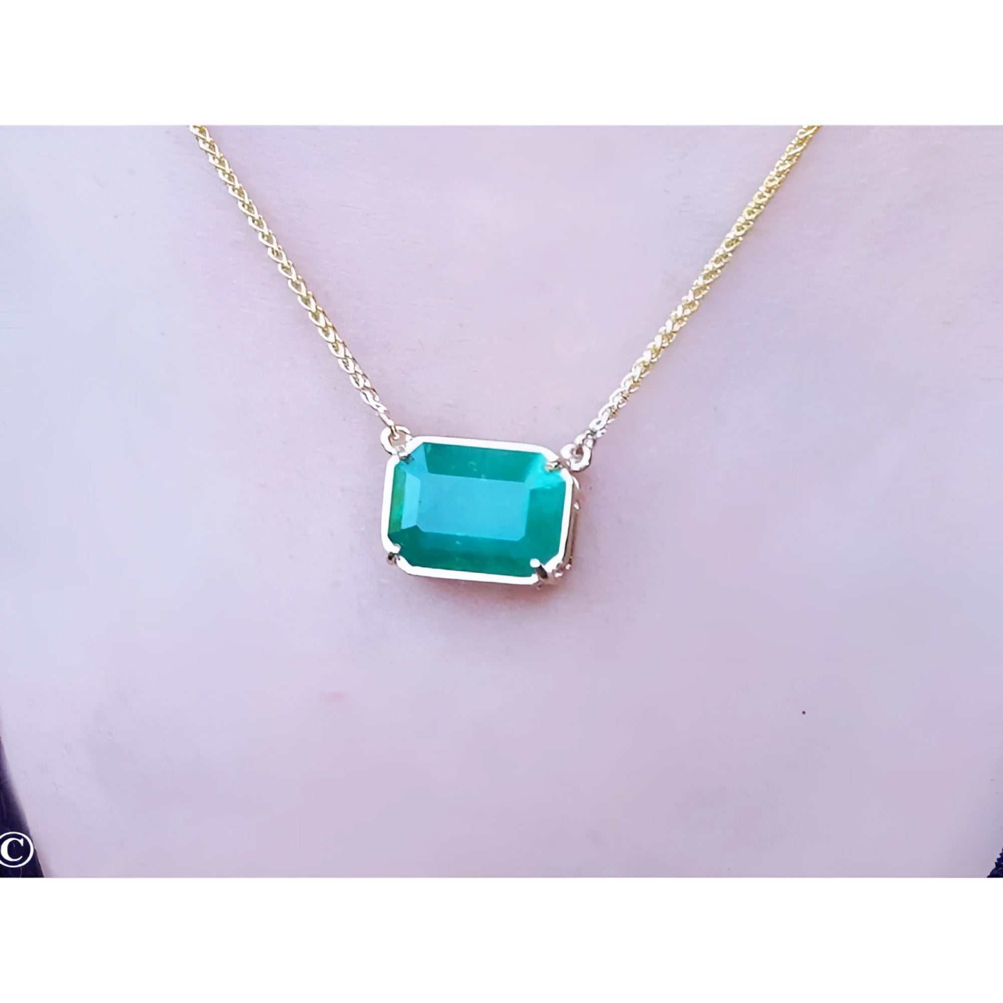 Emerald-cut Colombian emerald solitaire necklace in 18K yellow gold, worn on a person.
