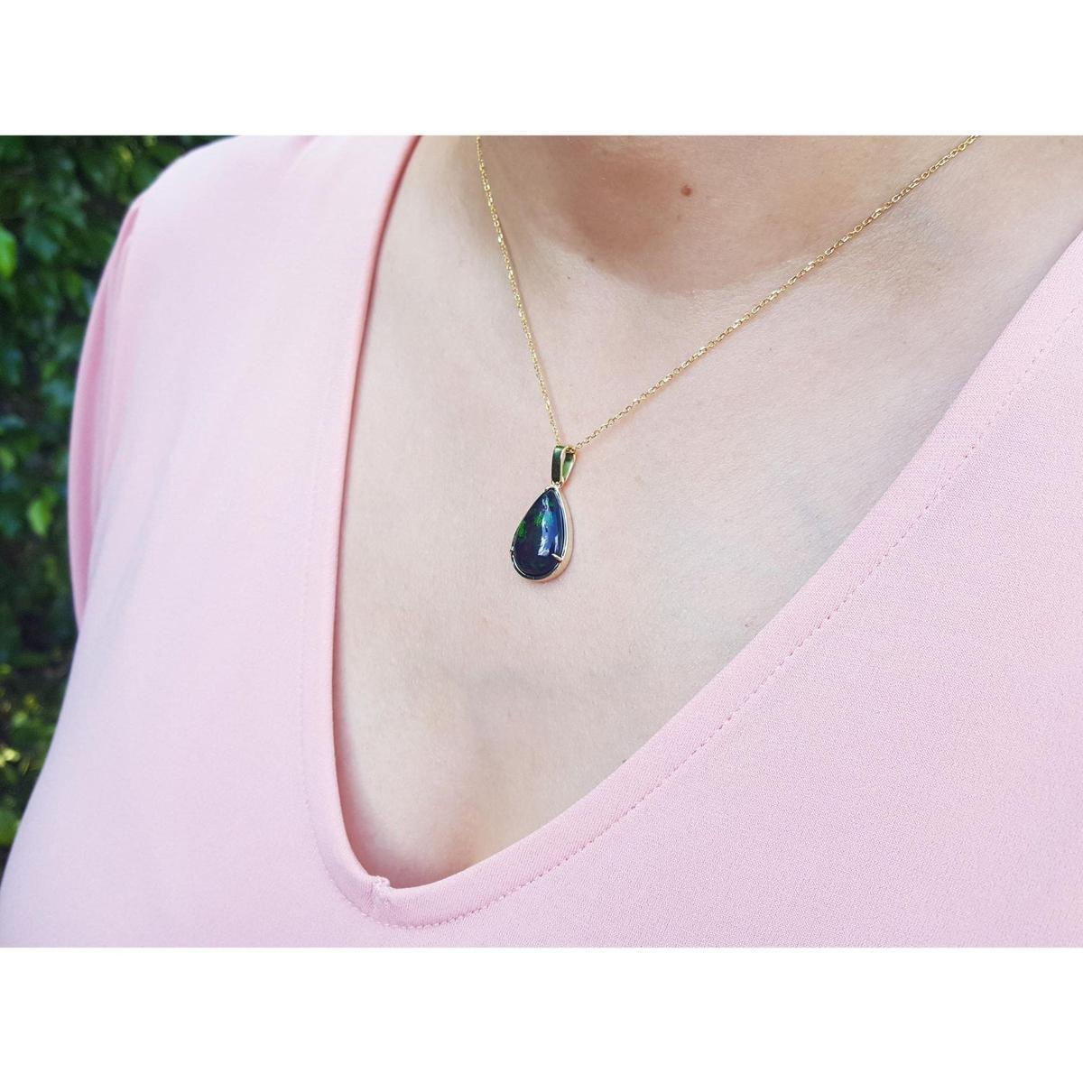 Teardrop-shaped black opal pendant on a gold chain worn by a person in a pink top.