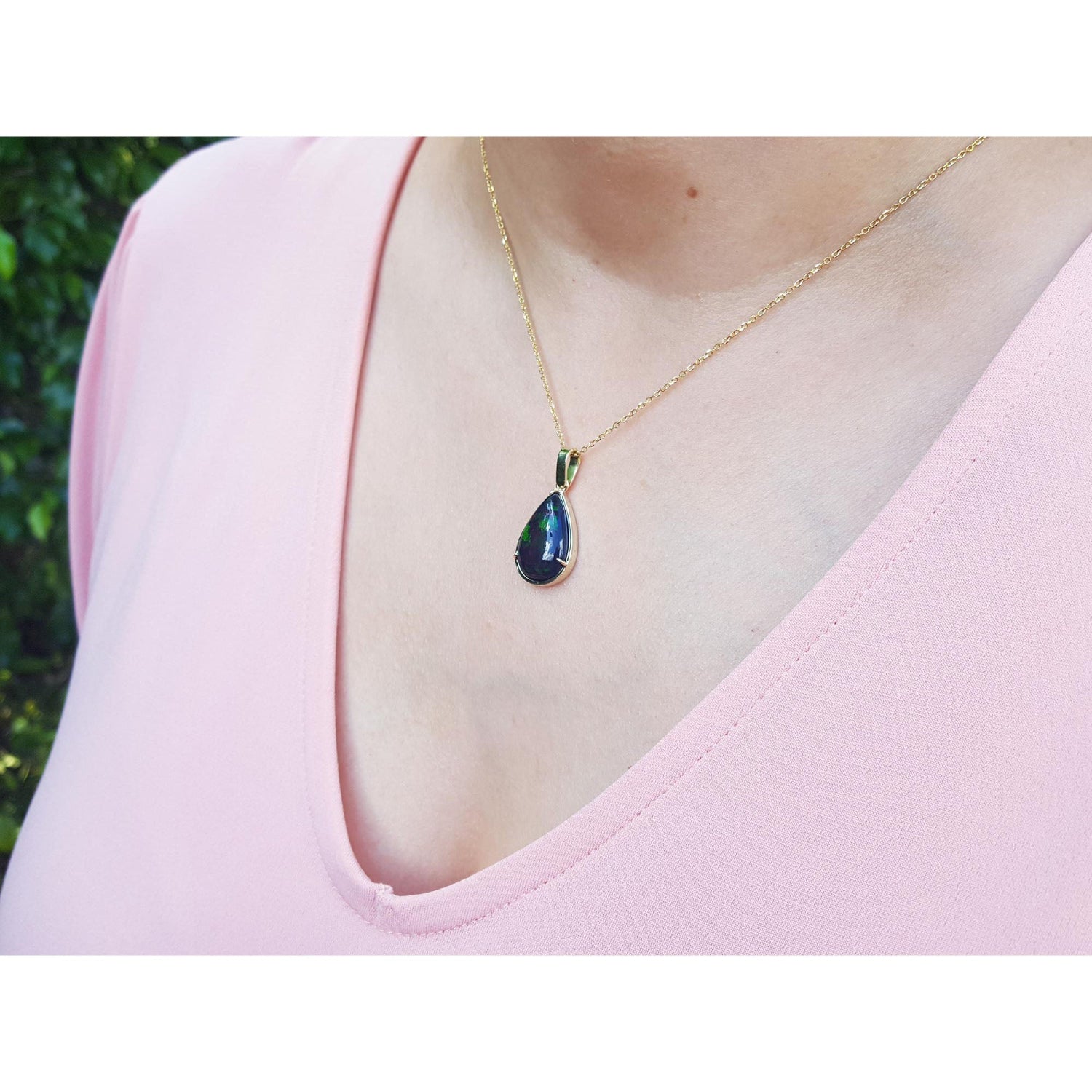 Teardrop-shaped black opal pendant on a gold chain worn by a person in a pink top.