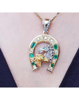 18K yellow gold horseshoe pendant with emeralds, diamonds, and two horse heads.
