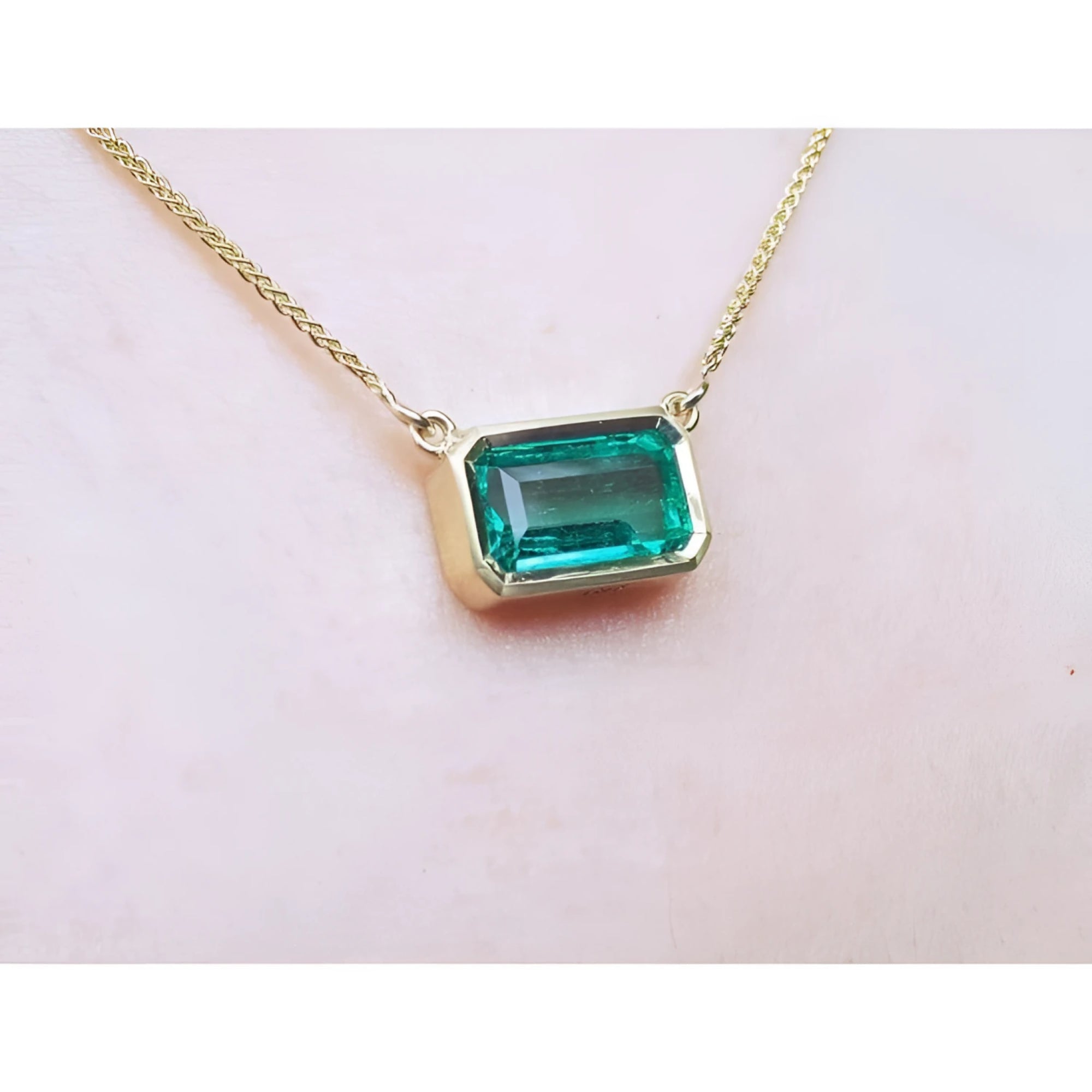 East-west emerald-cut solitaire emerald necklace in 18K yellow gold, bezel set.