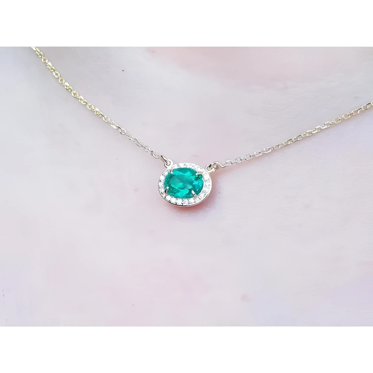 Oval Muzo emerald necklace with diamond halo on a delicate 14K yellow gold chain.