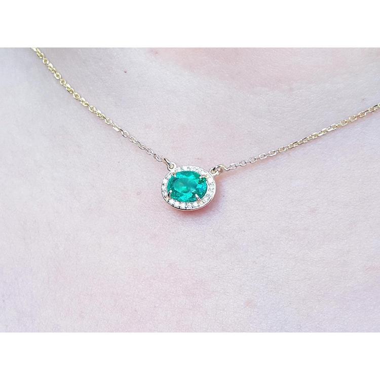 Oval Muzo emerald necklace with diamond halo on a delicate 14K yellow gold chain.