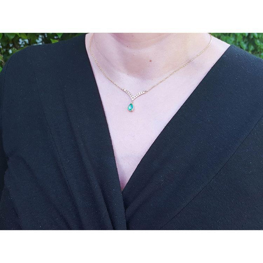 14K yellow gold necklace with a pear-cut emerald and diamond V-chevron pendant on a woman's neck.