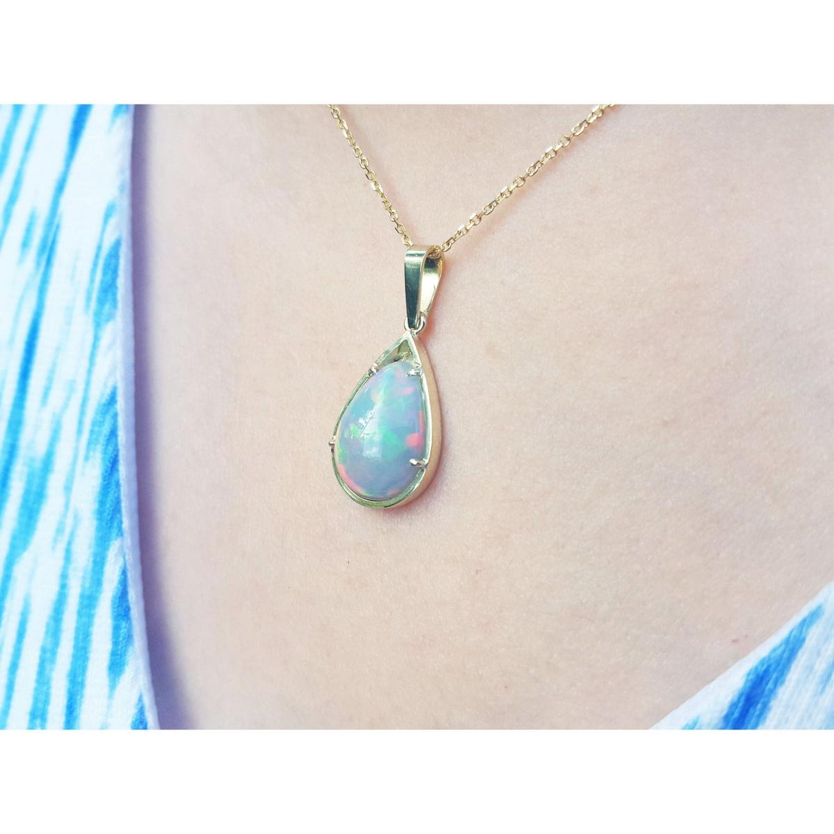 Opal pendant necklace on a person's neck wearing a blue and white patterned top.