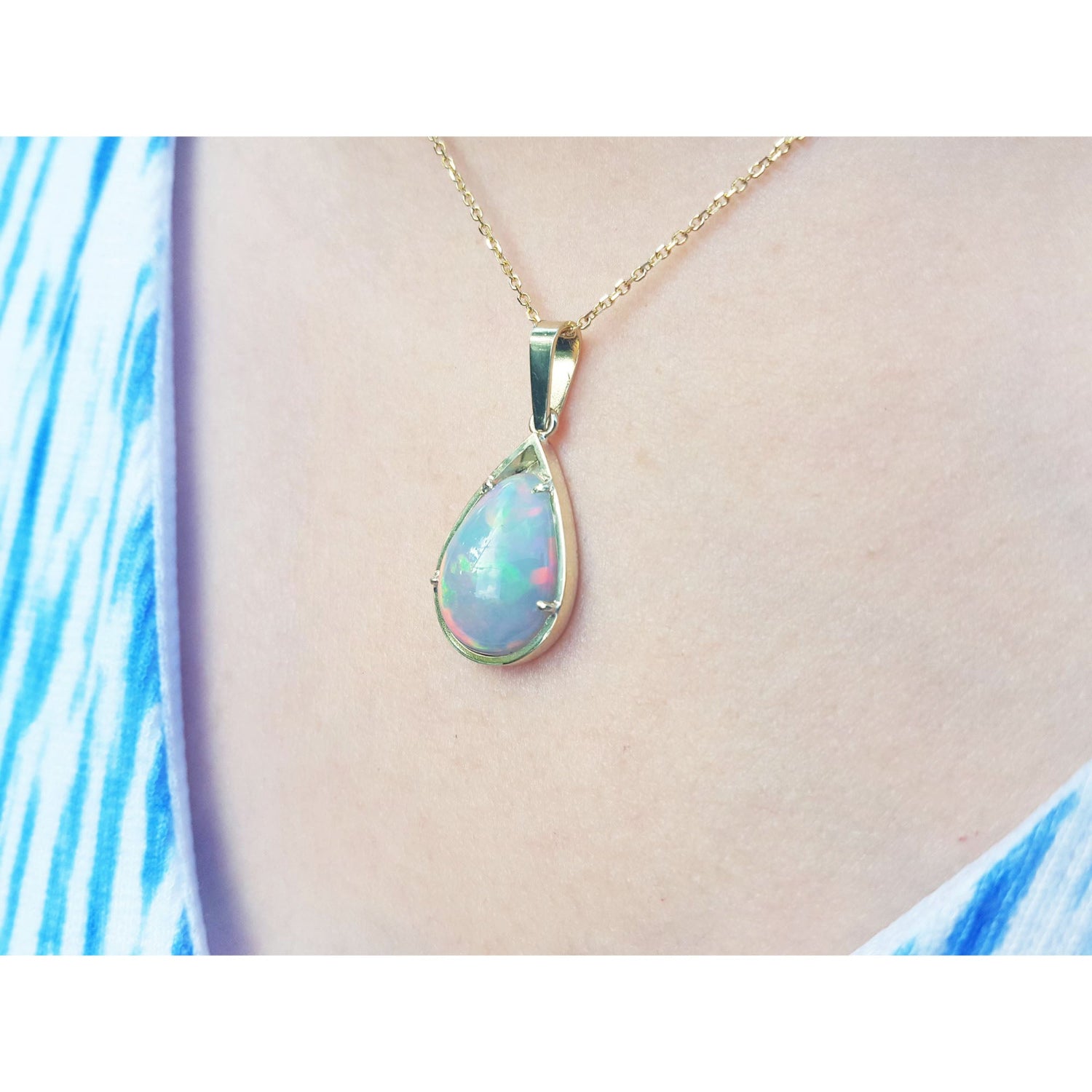 Opal pendant necklace on a person&#39;s neck wearing a blue and white patterned top.