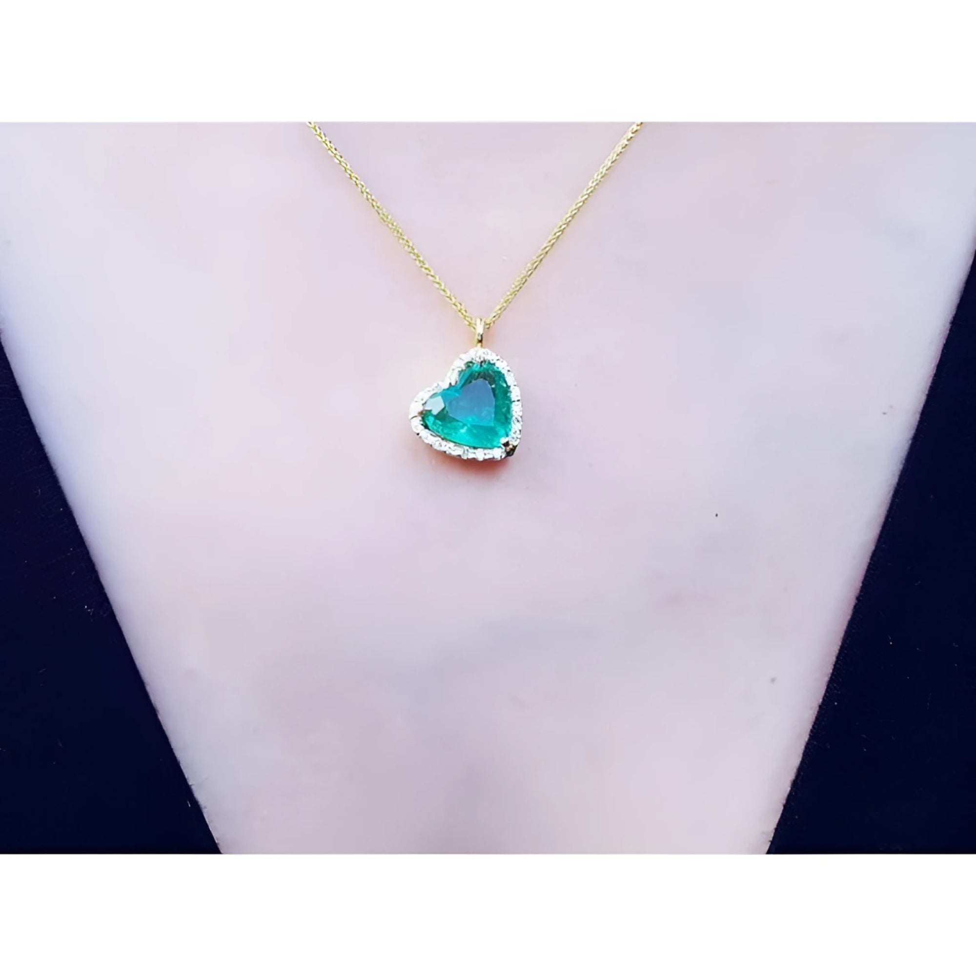 Tilted heart emerald necklace with halo diamonds on an 18K yellow gold chain.
