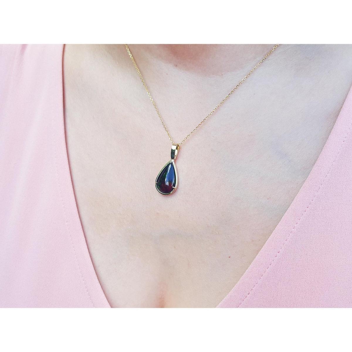 Teardrop-shaped black opal pendant necklace on a person's neck wearing a pink top.