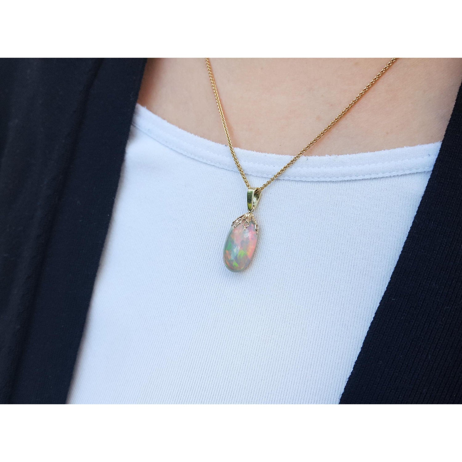 Opal pendant necklace on a person wearing a white top and black jacket.