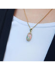 Opal pendant necklace on a person wearing a white top and black jacket.