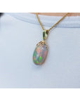 Opal pendant on a gold chain against a light blue background