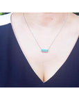 A lady wearing a natural emerald necklace with a halo diamond and white gold chain on a white background