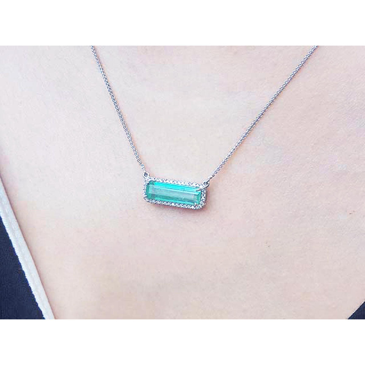 Elongated emerald necklace east-west orientation with a halo diamond pendant on a women&#39;s neck