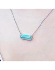 Elongated emerald necklace east-west orientation with a halo diamond pendant on a women's neck