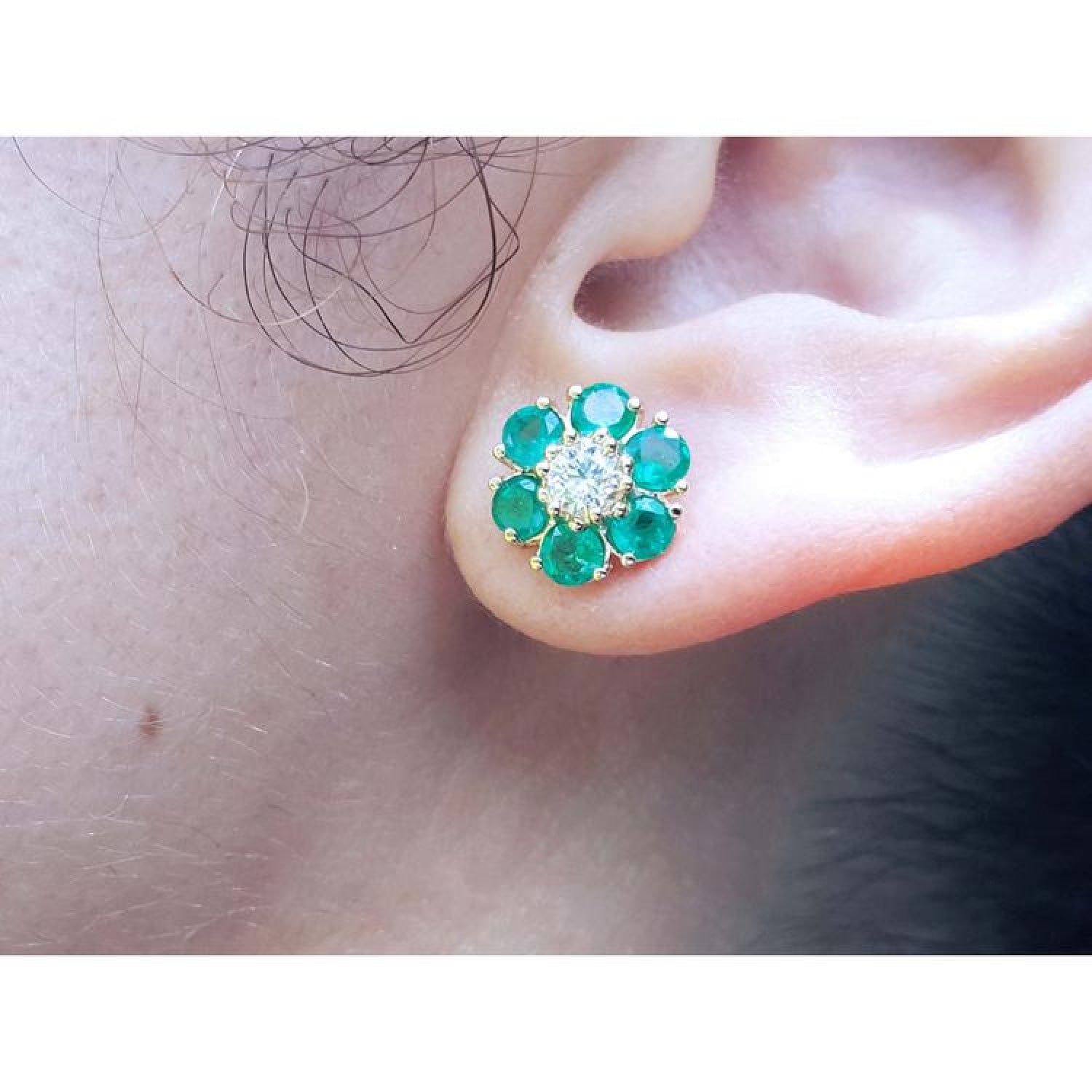 Colombian emerald and diamond cluster earring in 18K yellow gold, worn on an ear.