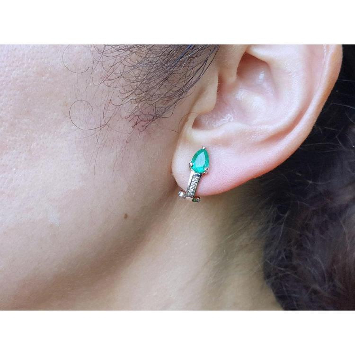 14K white gold clip-on earrings with pear-shaped emeralds and accent diamonds on an ear.