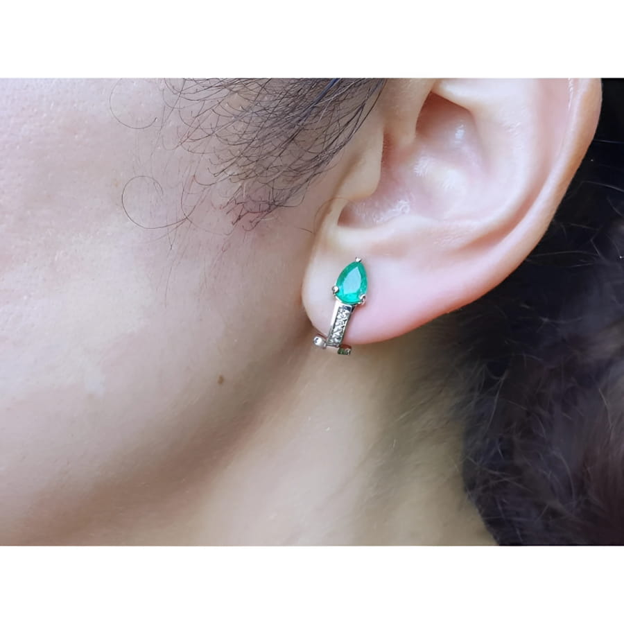 14K white gold clip-on earrings with pear-shaped emeralds and accent diamonds on an ear.