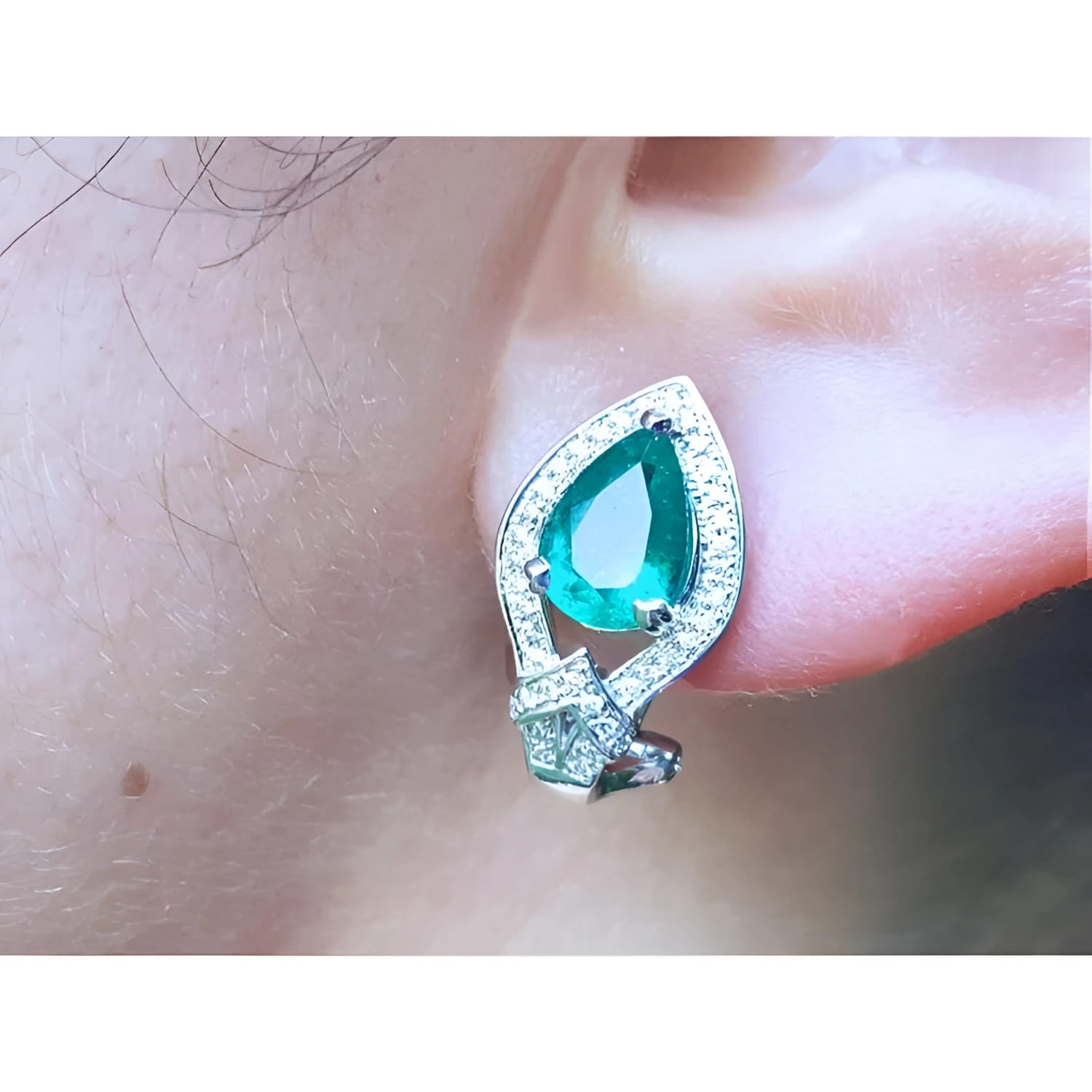 Close-up of a teardrop emerald earring clip-on system on an ear.