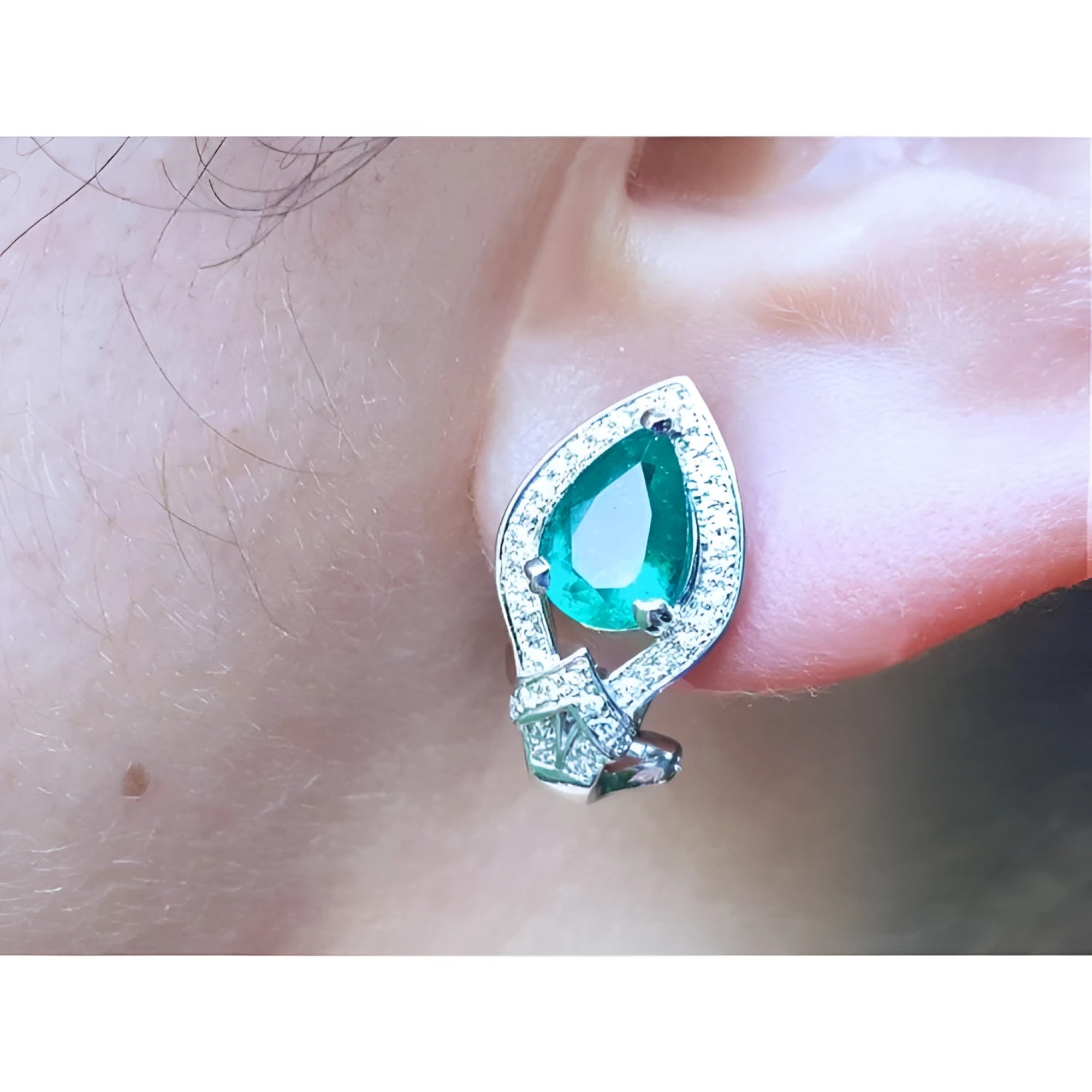 Close-up of a teardrop emerald earring clip-on system on an ear.
