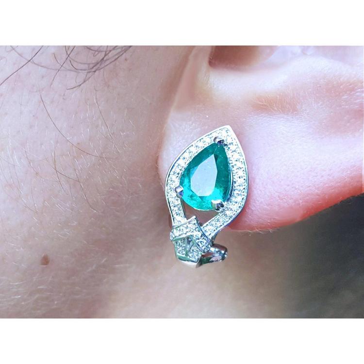 Close-up of a teardrop emerald earring clip-on system on an ear.