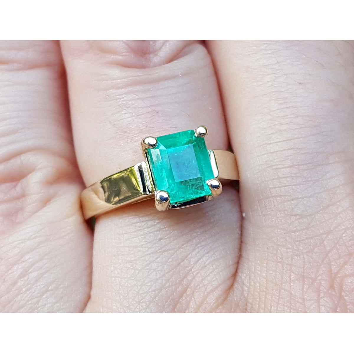 14k yellow gold genuine Muzo colombian emerald solitaire ring on a finger.