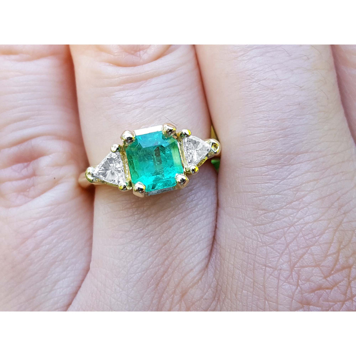 A Yellow gold 18k ring for women with a natural colombian emerald and trillion side diamonds. on a hand.