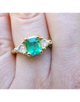 A Yellow gold 18k ring for women with a natural colombian emerald and trillion side diamonds. on a hand.