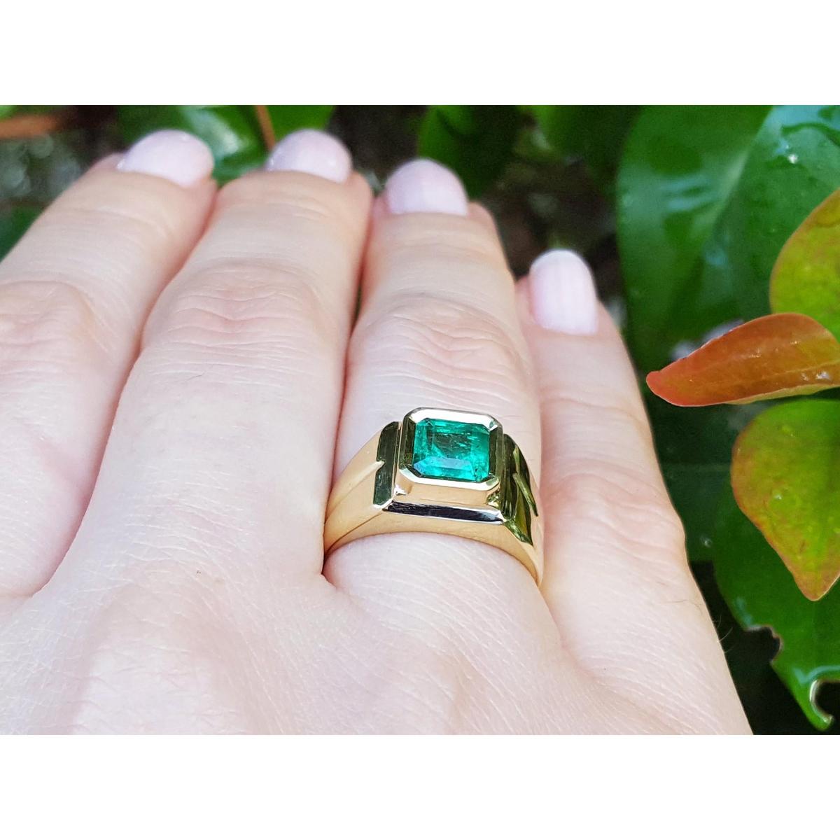 Gold ring with a bezel set emerald on a hand against a natural background