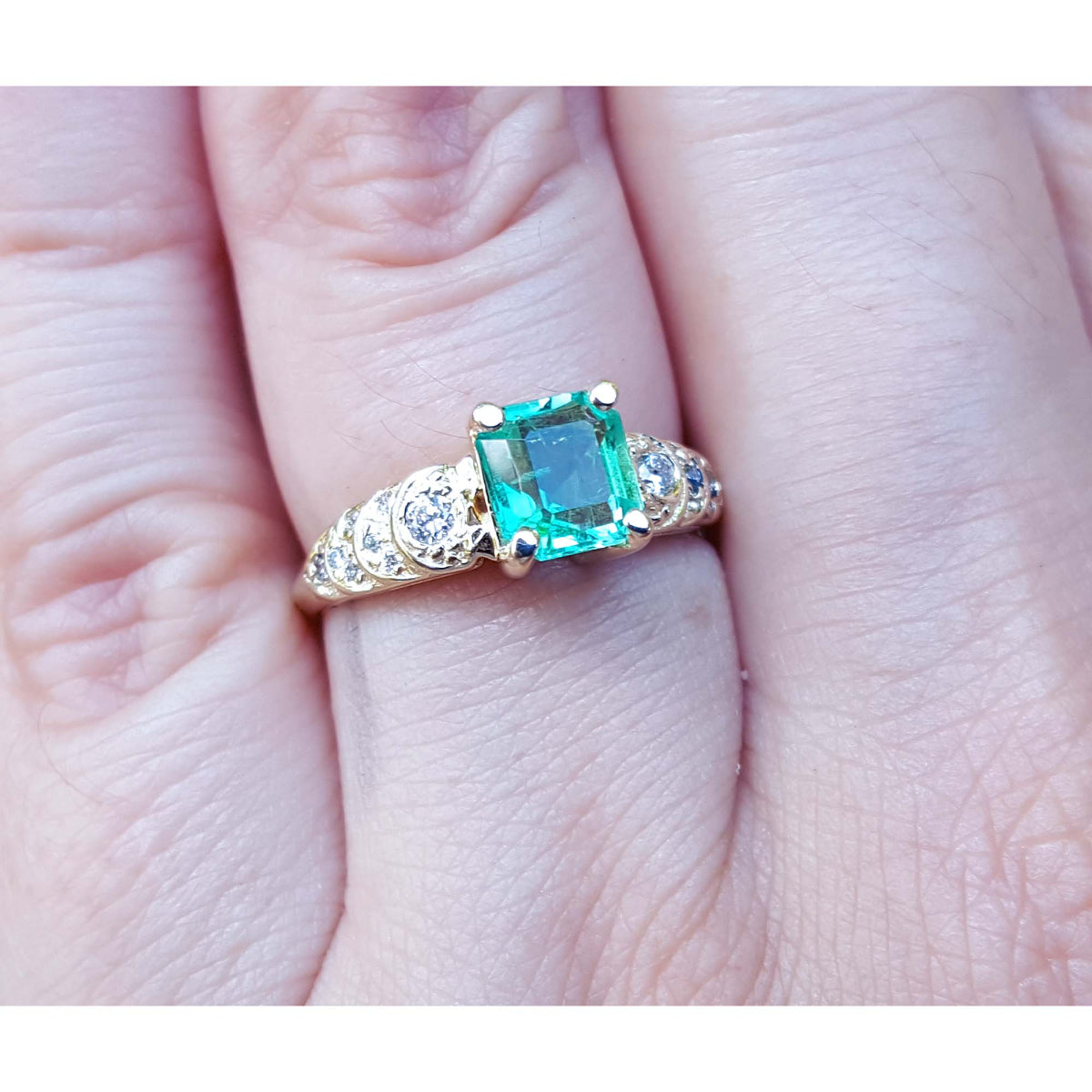 A 14k yellow gold natural colombian emerald ring for women on a finger.