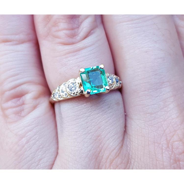 A 14k yellow gold natural colombian emerald ring for women on a finger.