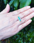 Emerald baguette cut necklace displayed on a woman's hand against a green leafy background