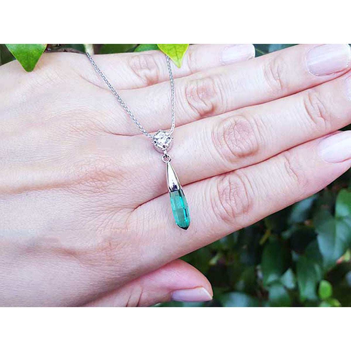 Colombian emerald briolette necklace with a green teardrop pendant held in a hand against a blurred green background