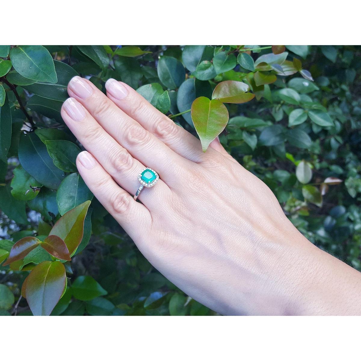 A hand wearing a cushion cut natural colombian emerald ring on a leafy background.