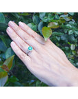 A hand wearing a cushion cut natural colombian emerald ring on a leafy background.