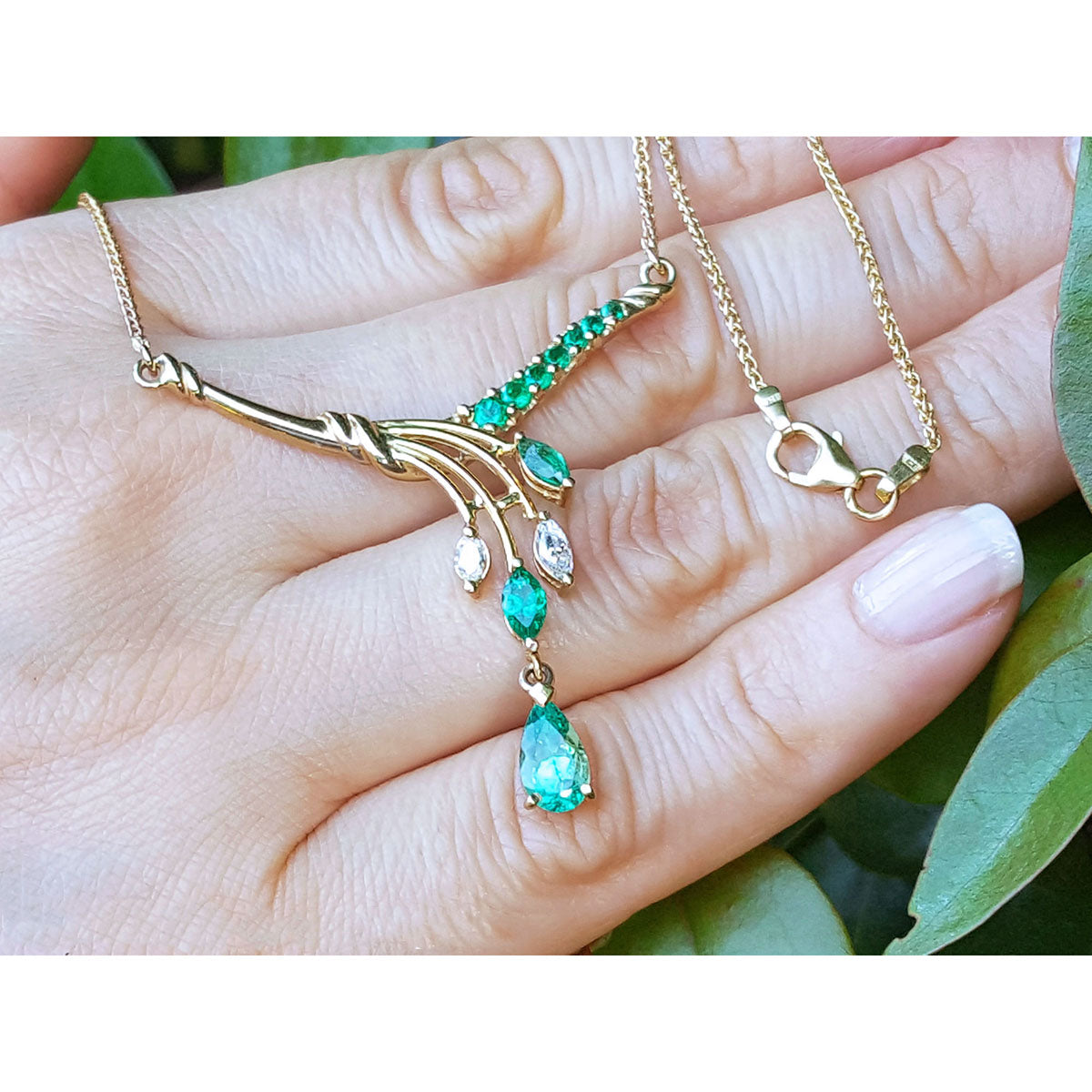Displaying a yellow gold necklace with real emeralds and diamonds gemstones held in a hand against a natural background