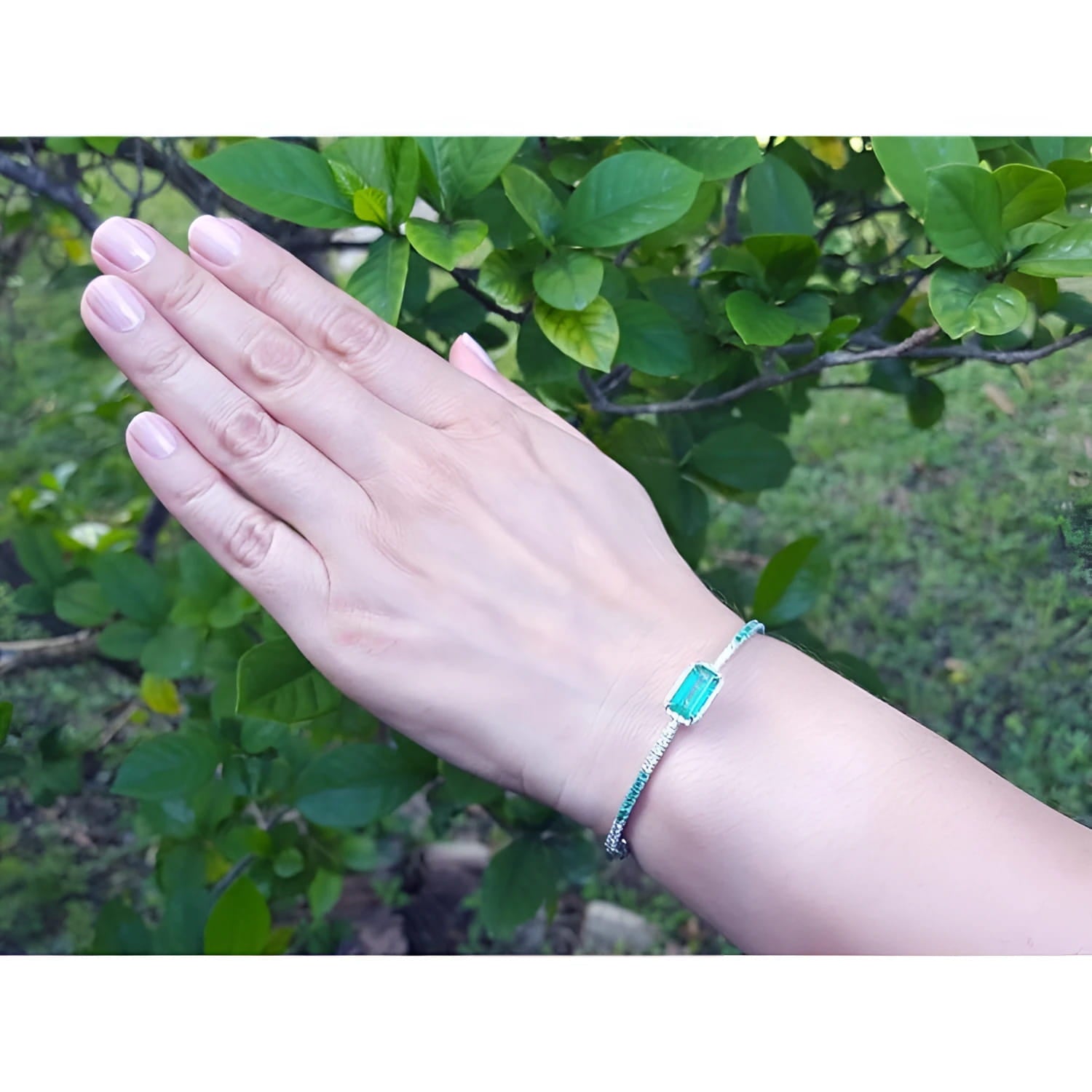 Emerald-cut Colombian emerald bangle bracelet with natural diamonds in 14K white gold on a hand.