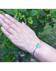 Hand wearing a natural emerald and diamond bangle bracelet with a green leafy background.