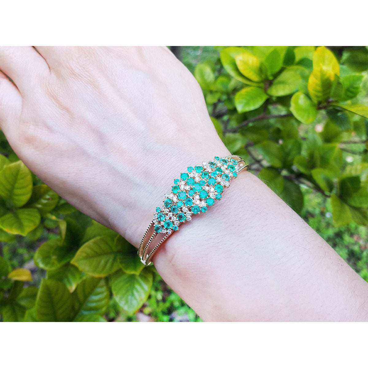 An emerald bangle bracelet on a wrist with a green leafy background.