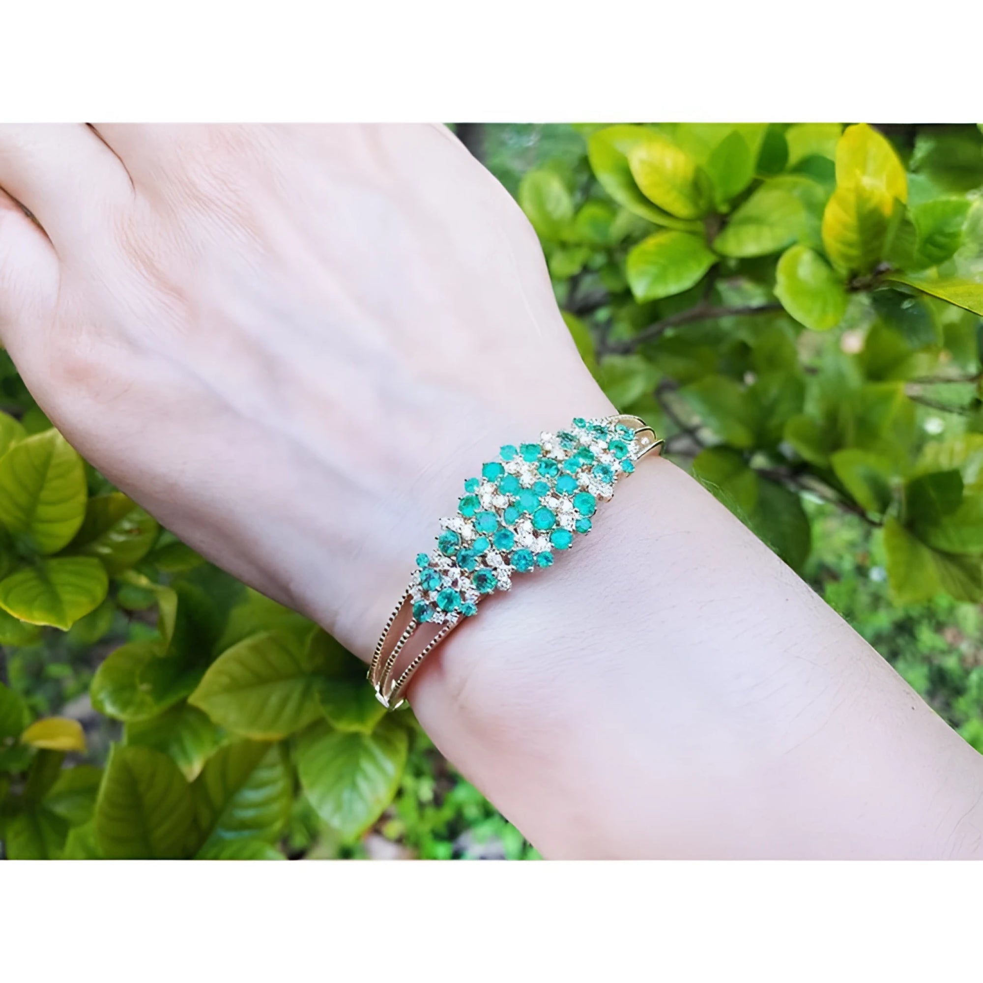 14K yellow gold bangle with round cut Colombian emeralds and diamonds in a floral design.