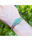 An emerald bangle bracelet on a wrist with a green leafy background.