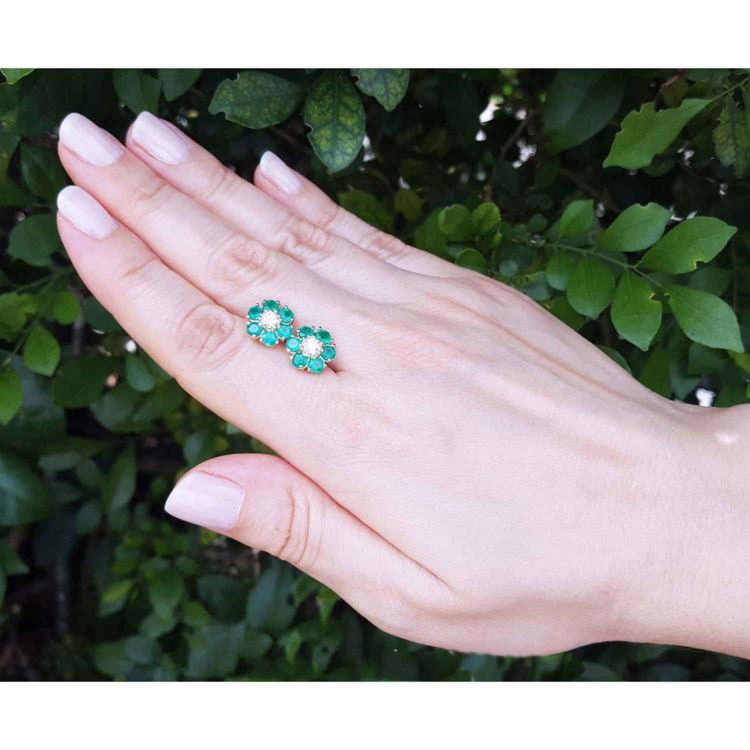18K yellow gold Colombian emerald and diamond cluster earrings on a hand.