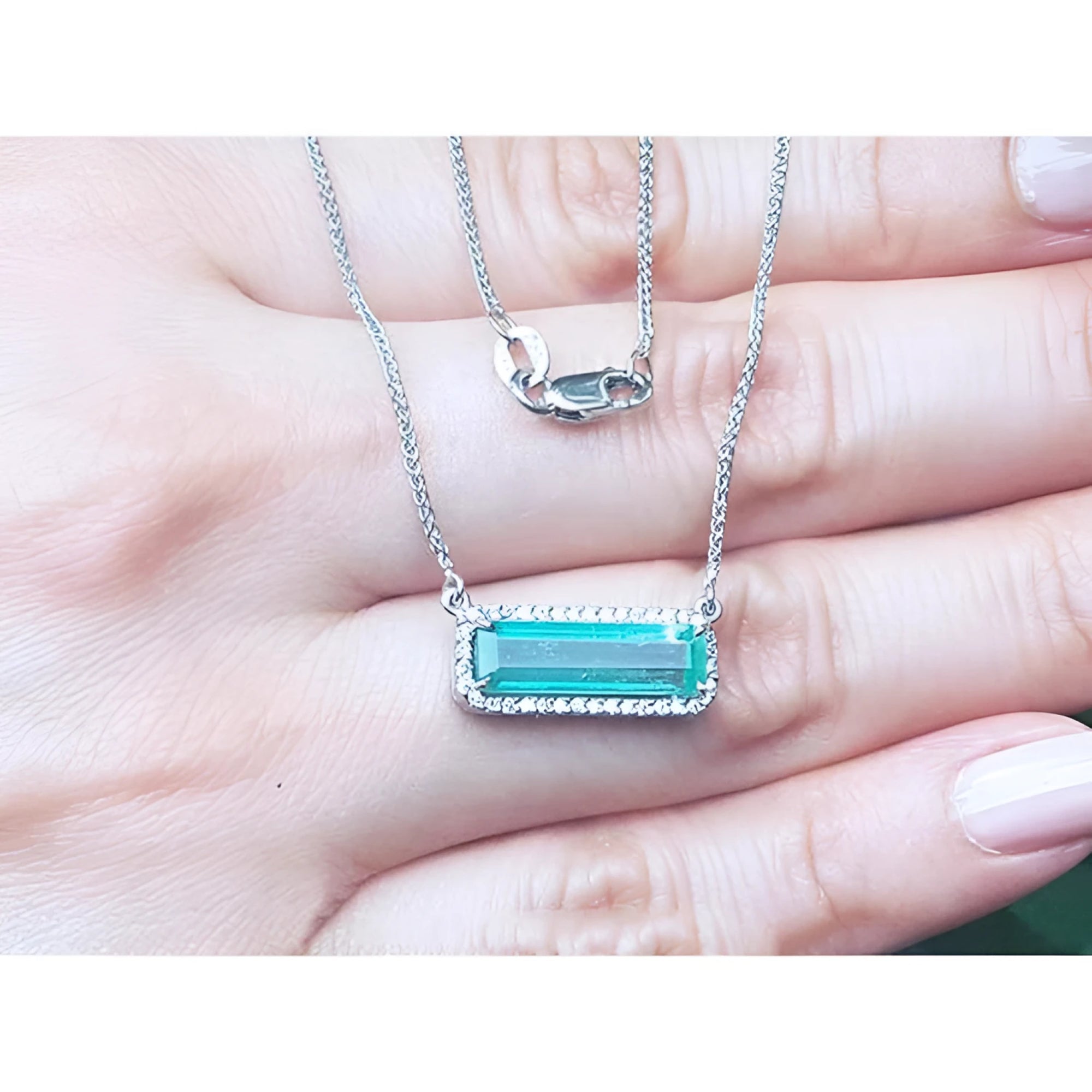 18K white gold necklace with a rectangular emerald-cut Colombian emerald and halo diamonds.