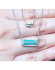 woman's hand showing a halo diamond Emerald necklace elongated east west orientation in 18k white gold