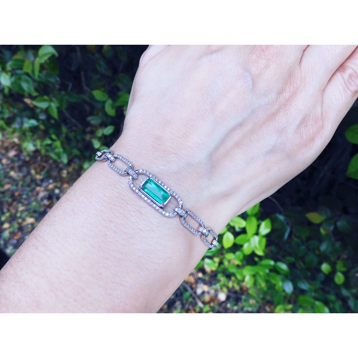 A paperclip gold bracelet with a real emerald on a wrist against a natural background.