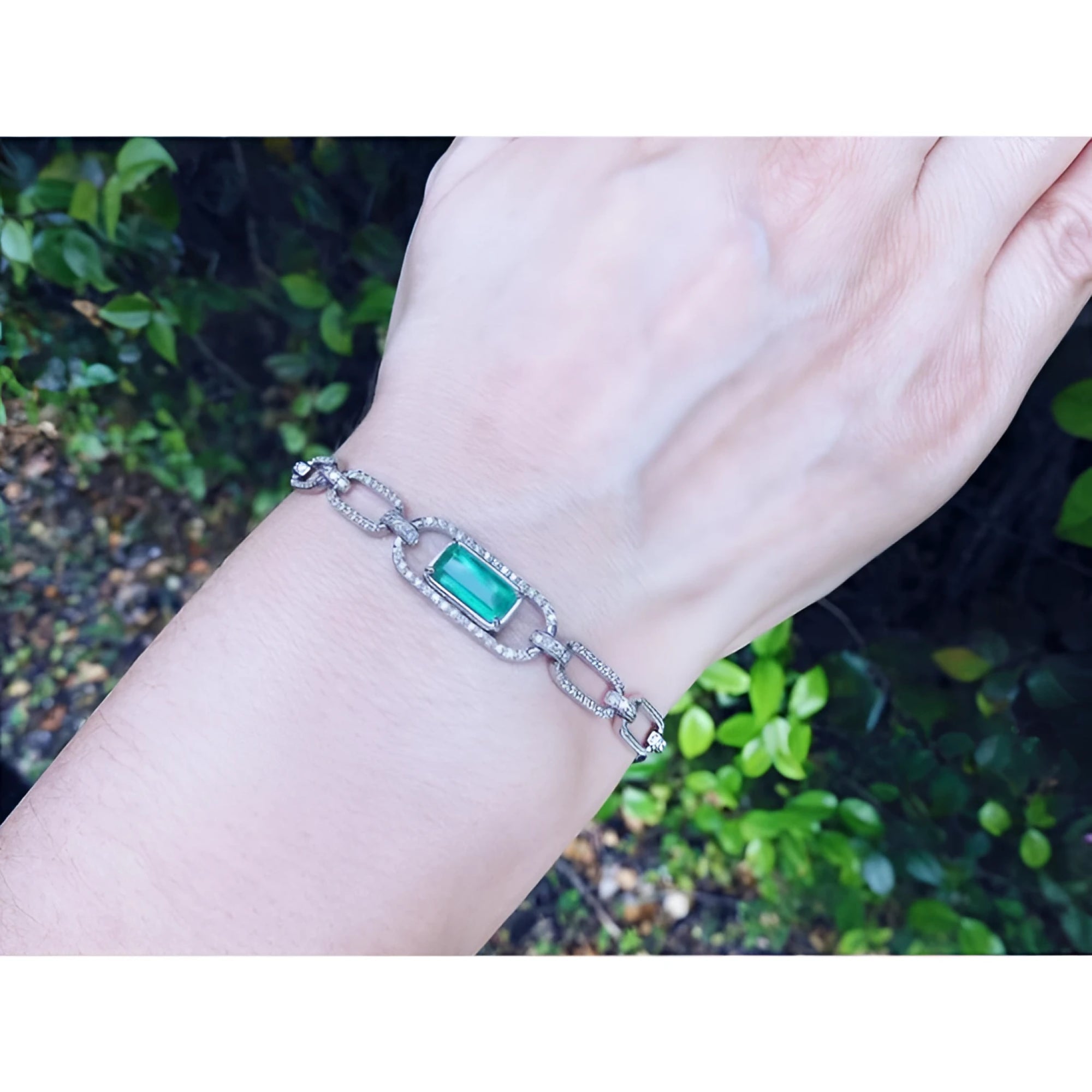 14K white gold paperclip bracelet with a vibrant emerald-cut emerald and diamond halo, worn on a wrist.