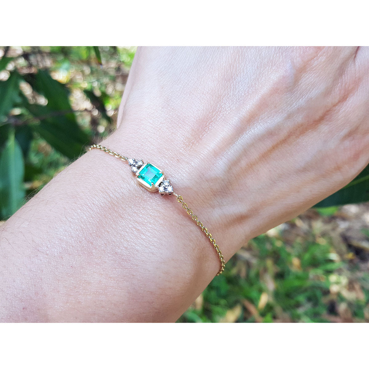 Gold bracelet with a real colombian emerald on a wrist against a natural background.